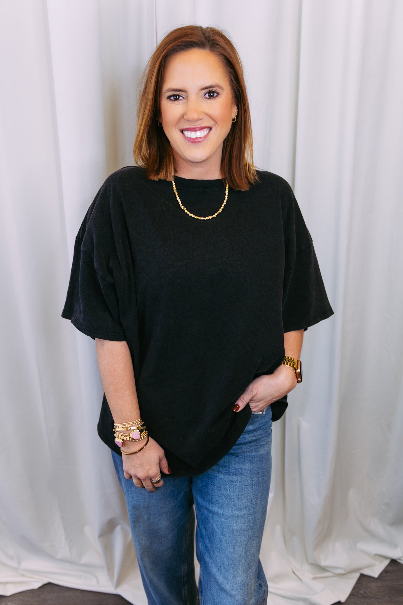 Woman wearing a black top and blue jeans against a white curtain background