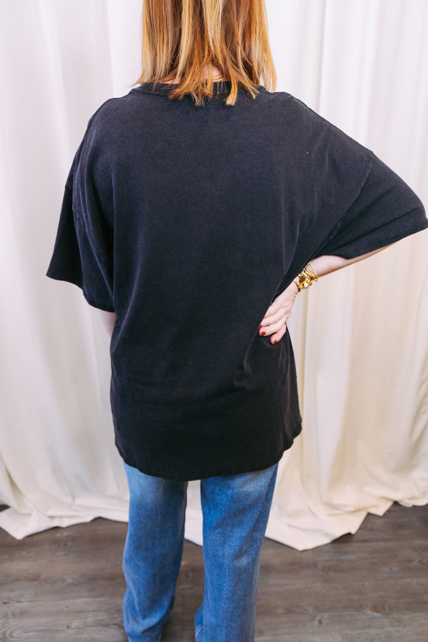 Person wearing a black oversized t-shirt and blue jeans with a white curtain background