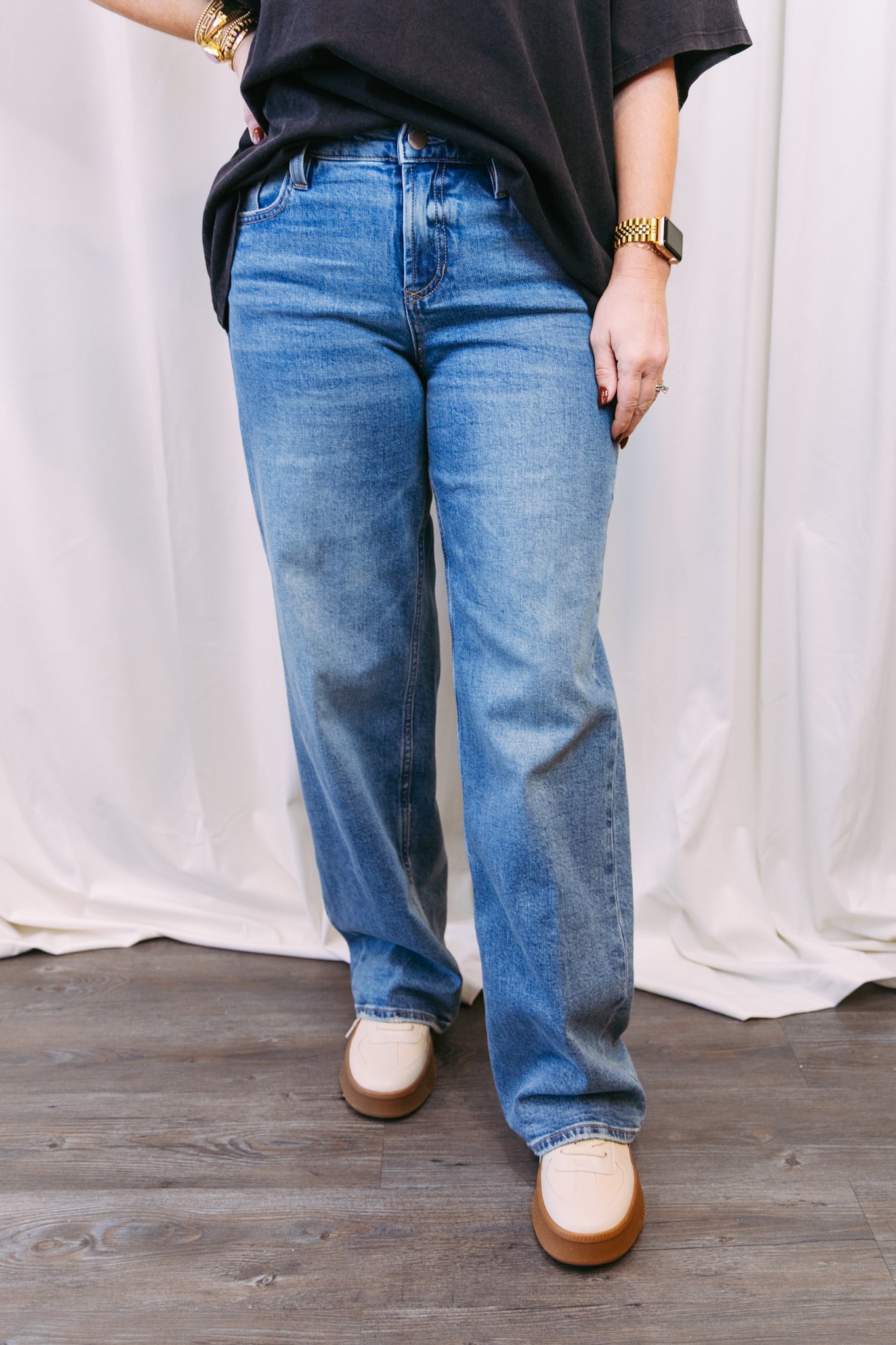 Person wearing blue jeans and a black top against a white curtain background