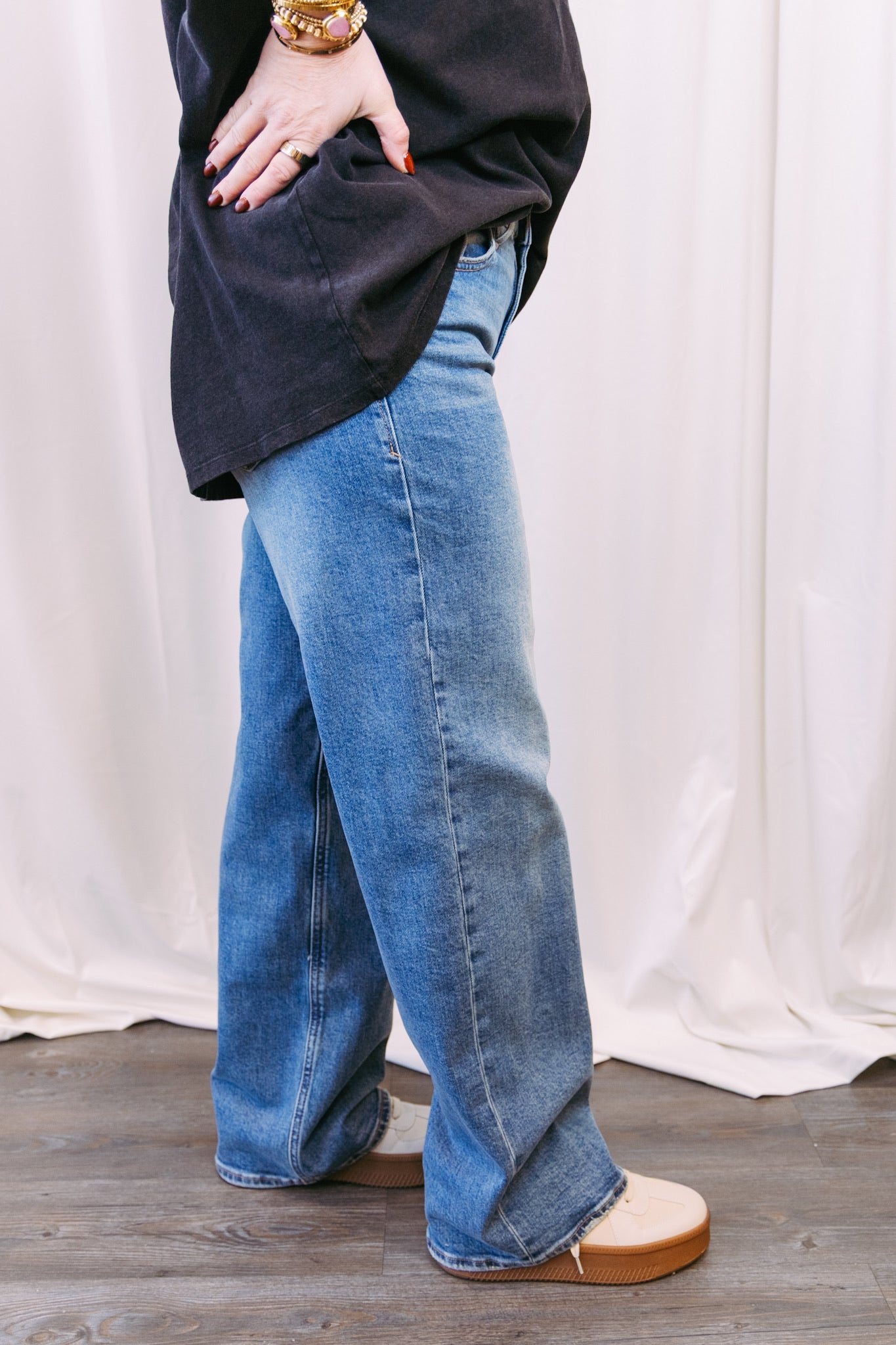 Person wearing blue jeans and a dark tshirt against a white curtain background