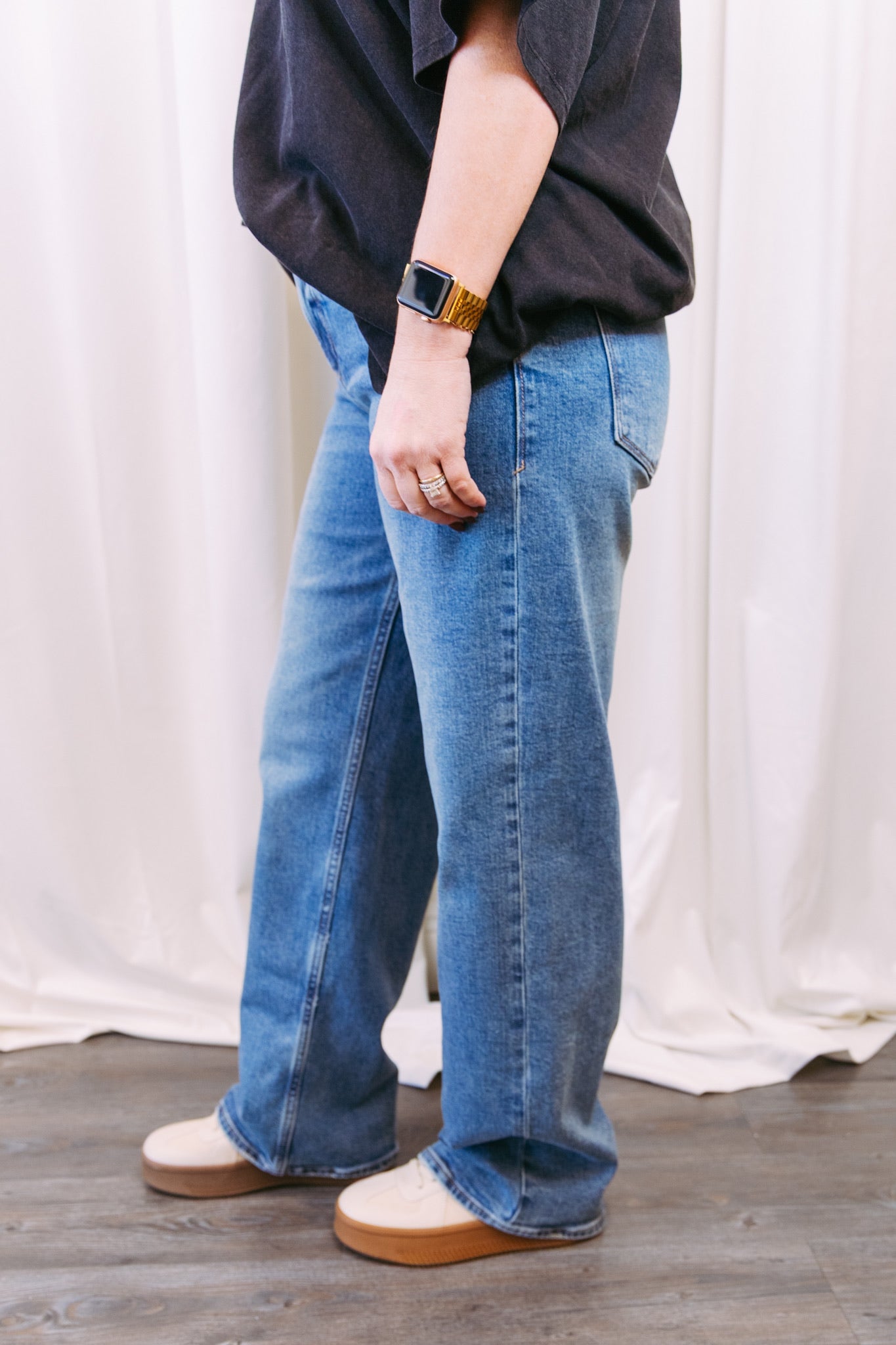 Person wearing blue jeans and a dark shirt against a white curtain background