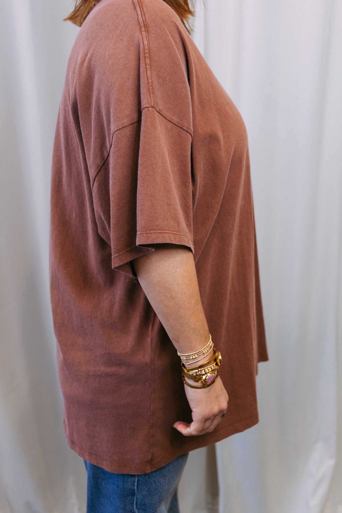 Person wearing a brown oversized shirt and blue jeans against a white background