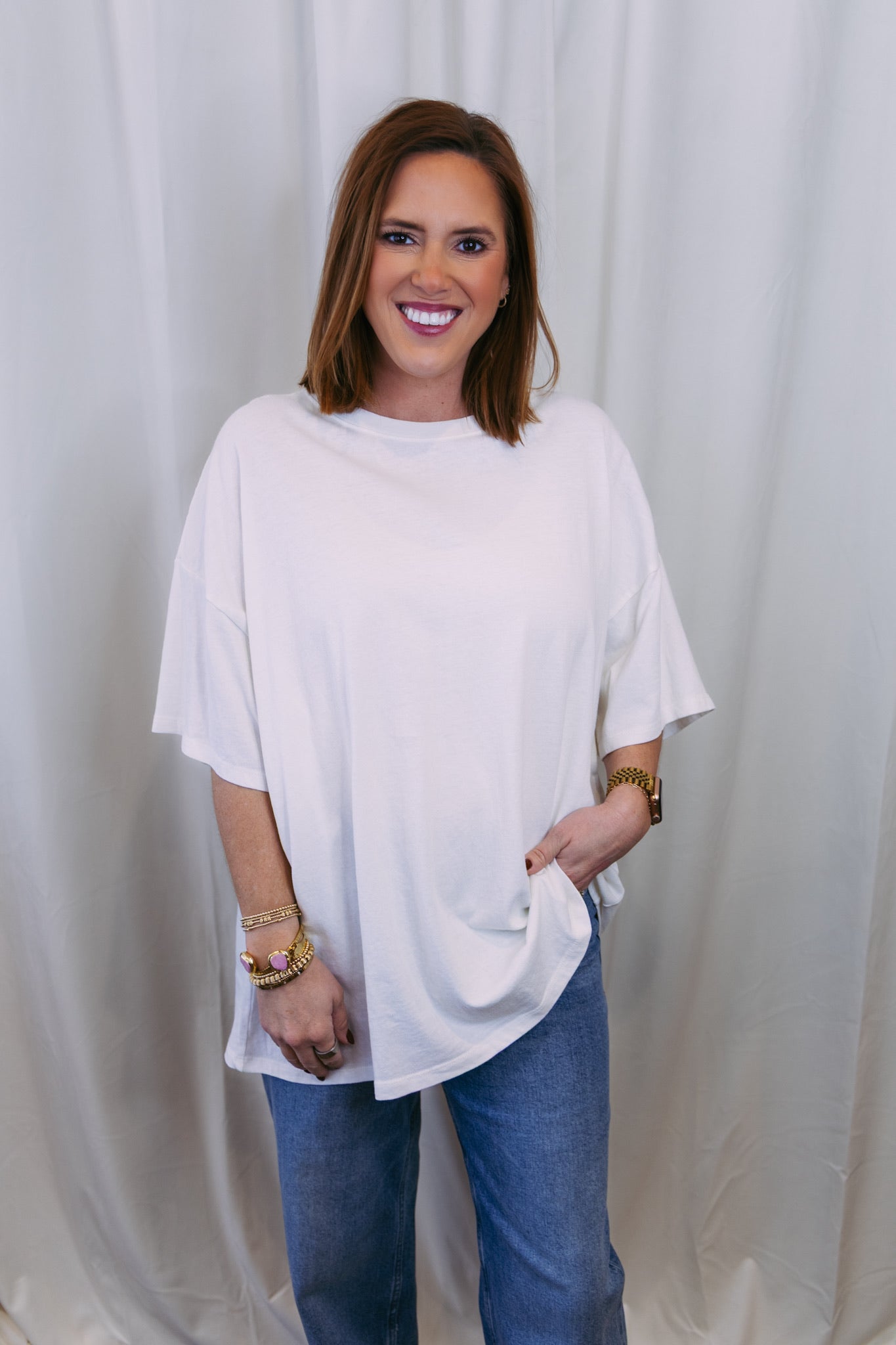 Woman wearing a white oversized shirt and blue jeans against a white curtain background