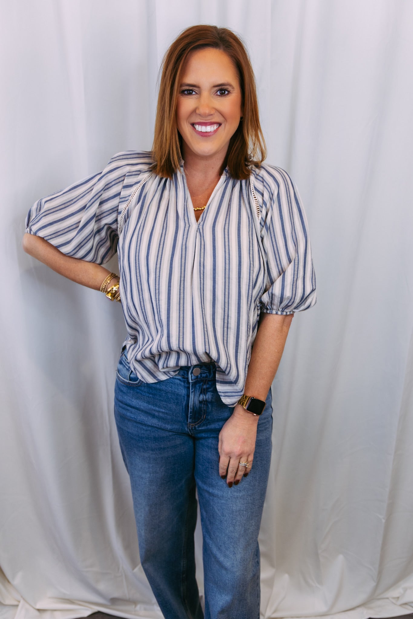 Woman wearing a striped blouse and jeans against a white curtain background