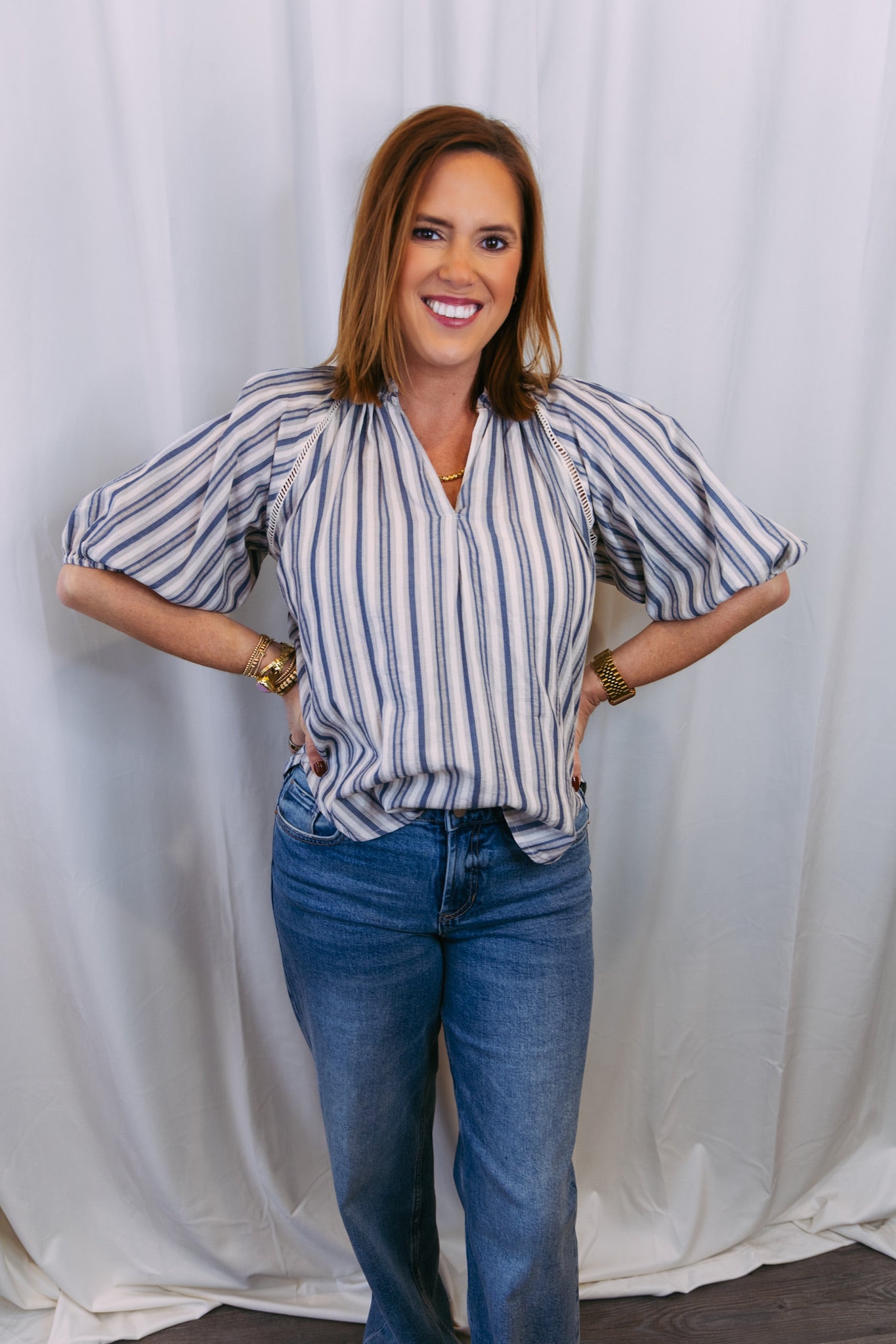 Woman wearing a striped shirt and blue jeans against a white curtain background