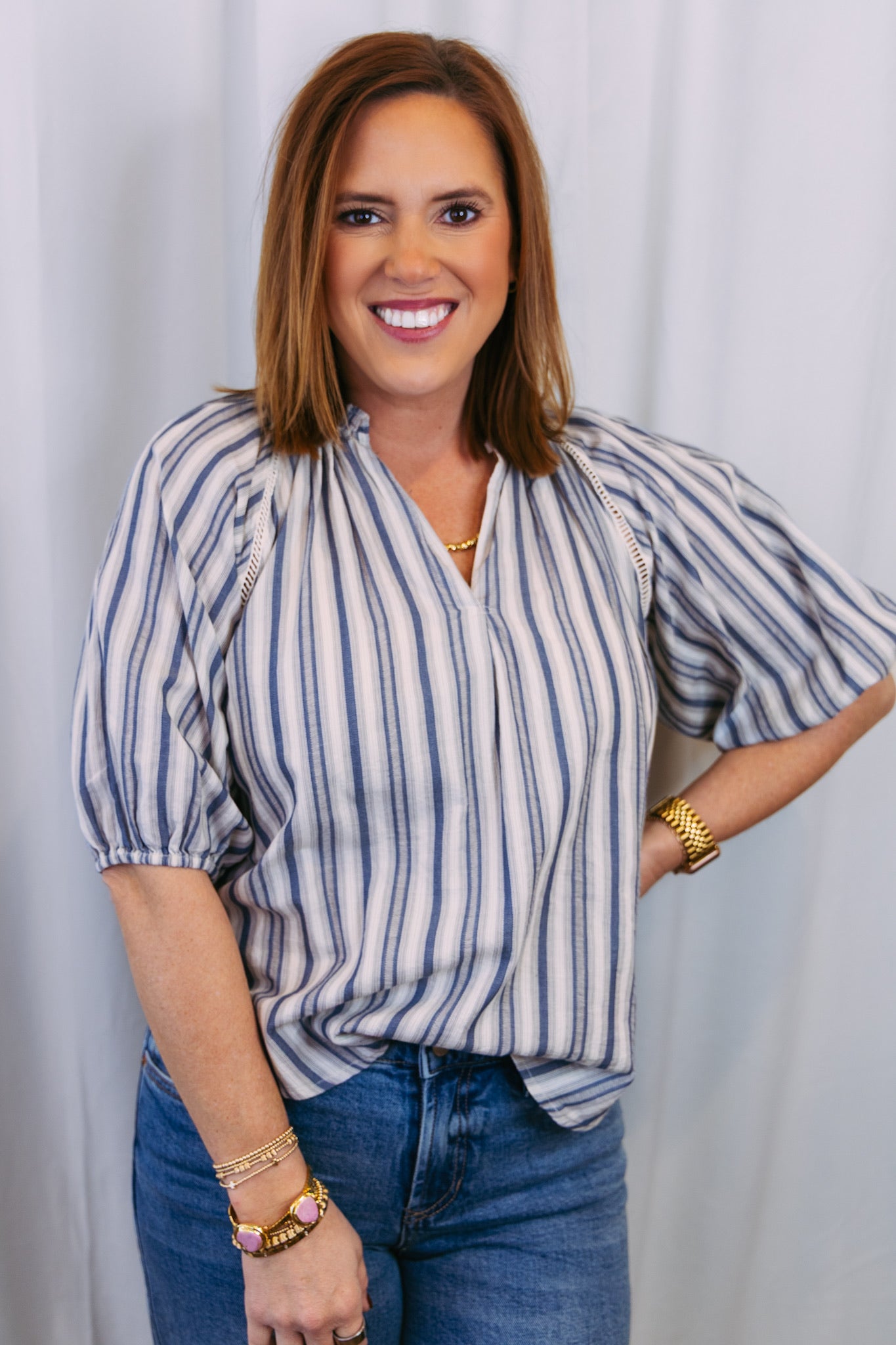 Woman wearing a striped blouse and jeans against a white curtain background