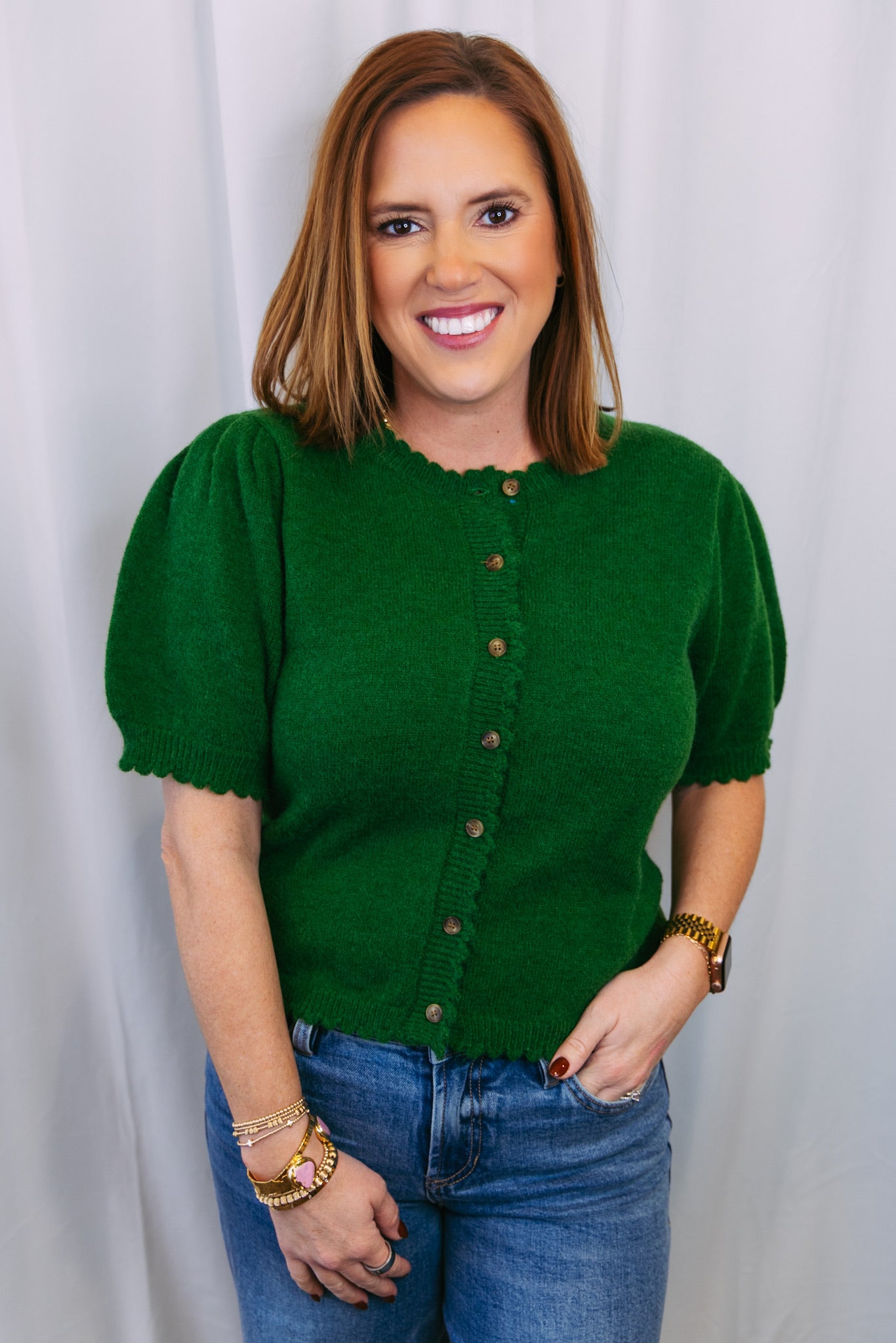 Woman wearing a green cardigan sweater and blue jeans against a white background