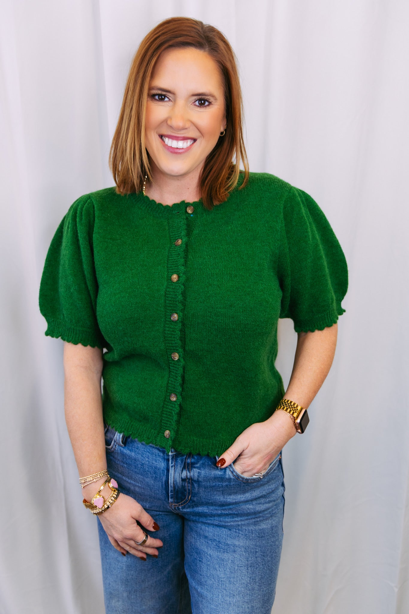 Woman wearing a green sweater with short sleeves and blue jeans against a white background