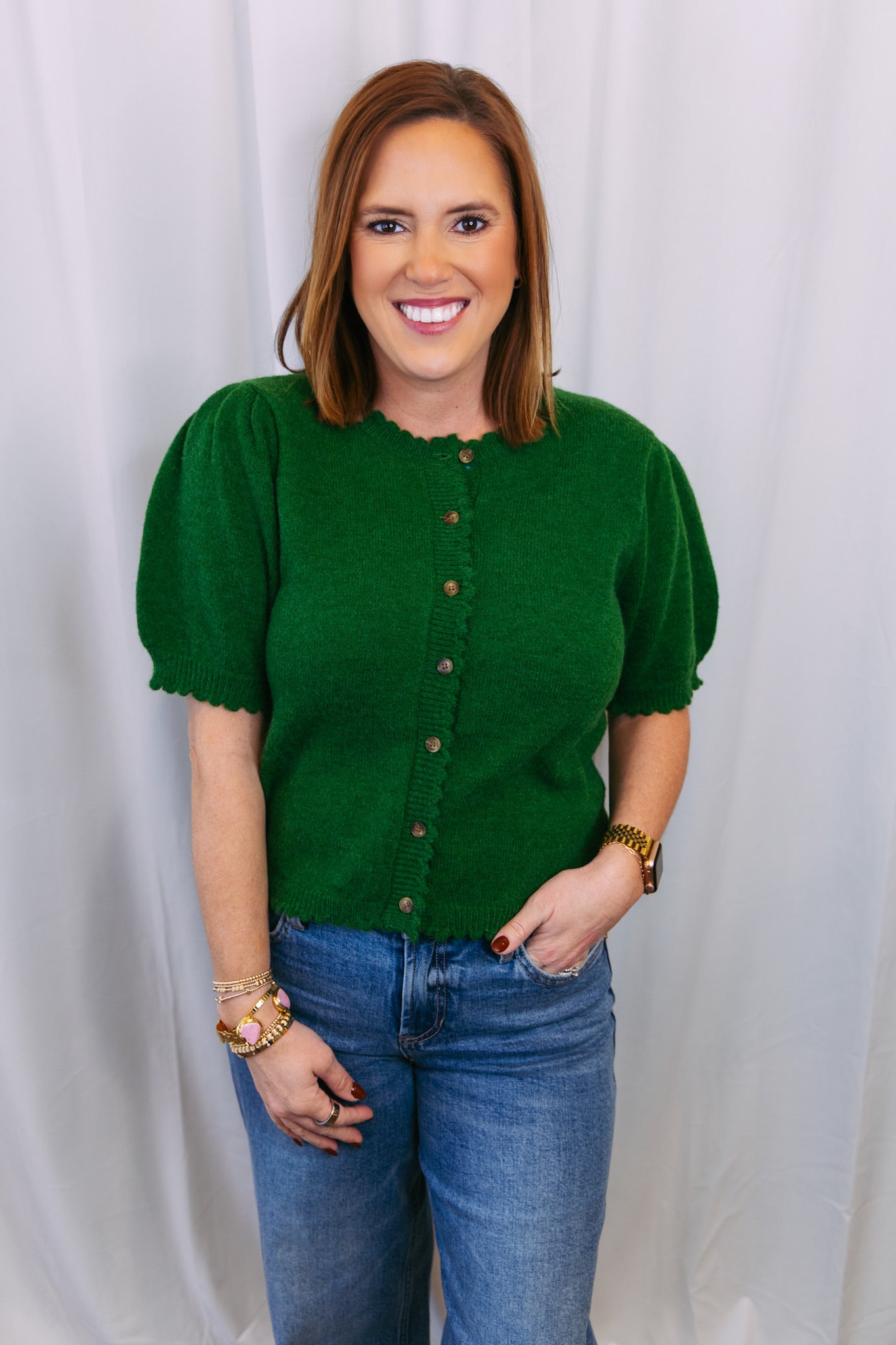 Woman wearing a green blouse with short sleeves and blue jeans against a white background