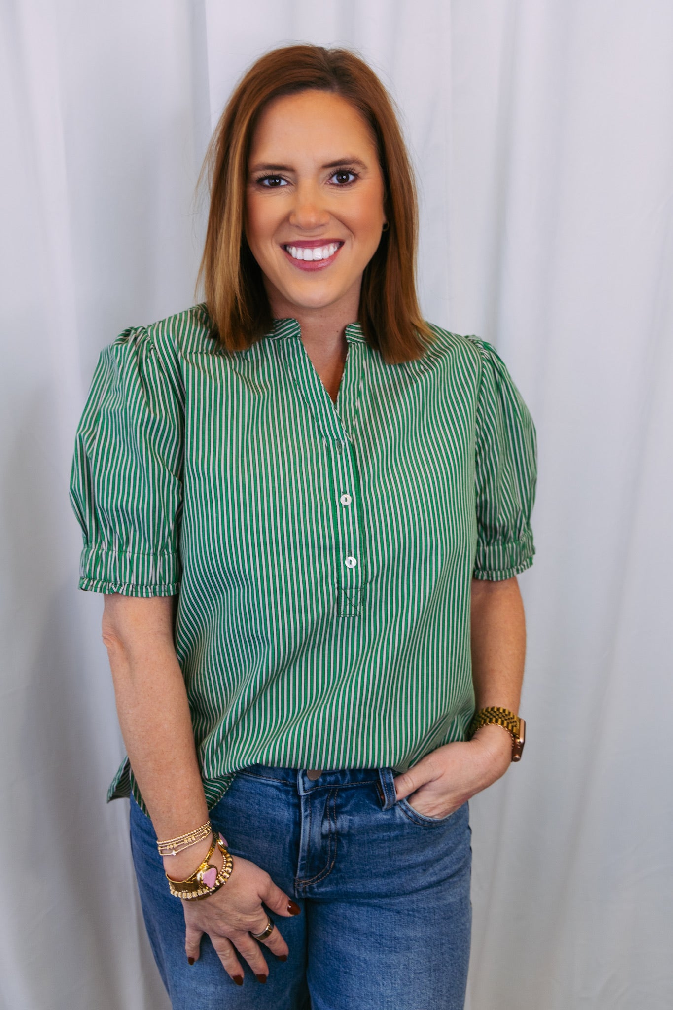 Woman wearing a green striped shirt and blue jeans against a white background
