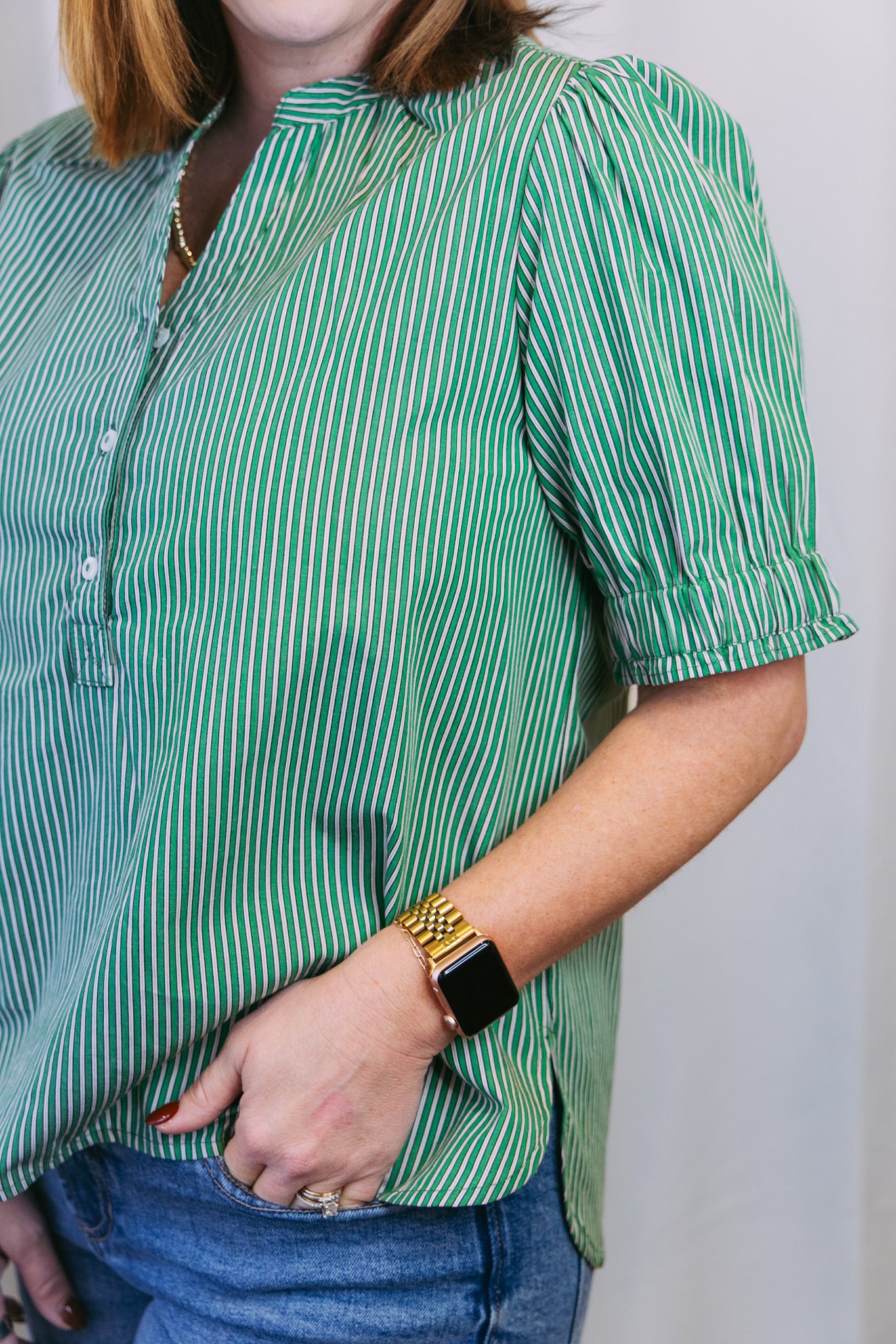 Person wearing a green and white striped shirt standing against a plain background.