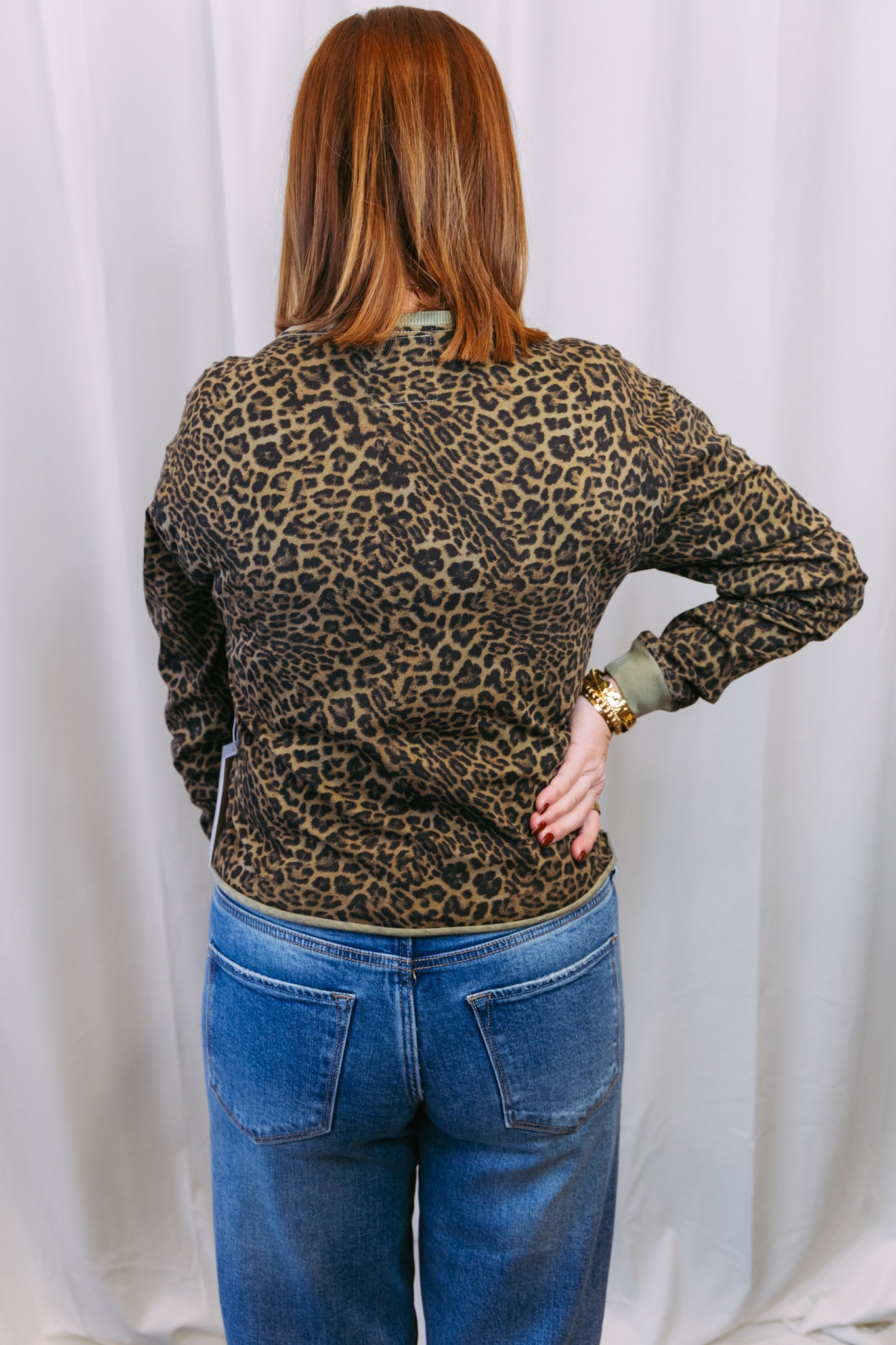 Person wearing a leopard print top and blue jeans against a white curtain background