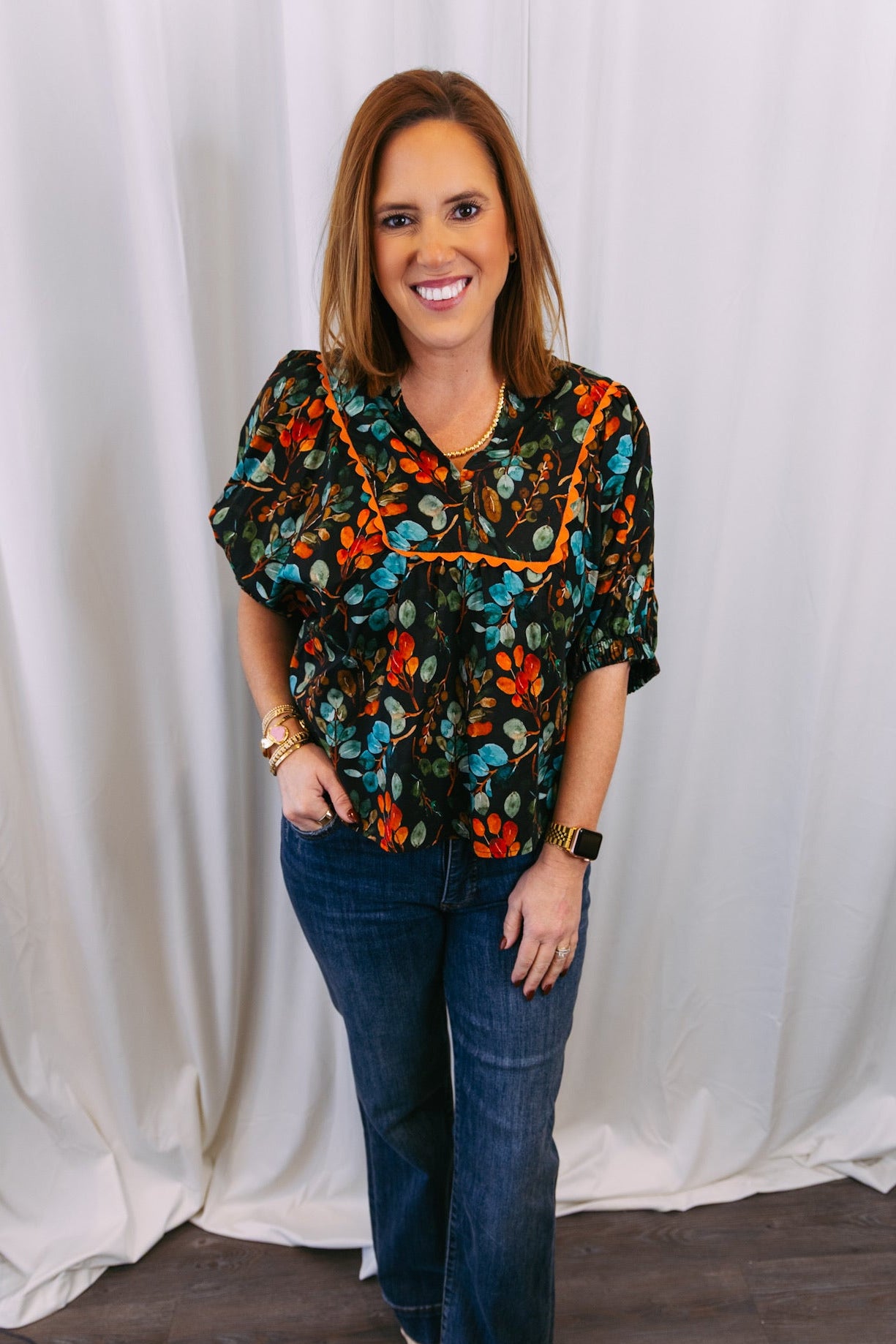 Woman wearing a floral blouse and jeans standing against a white curtain