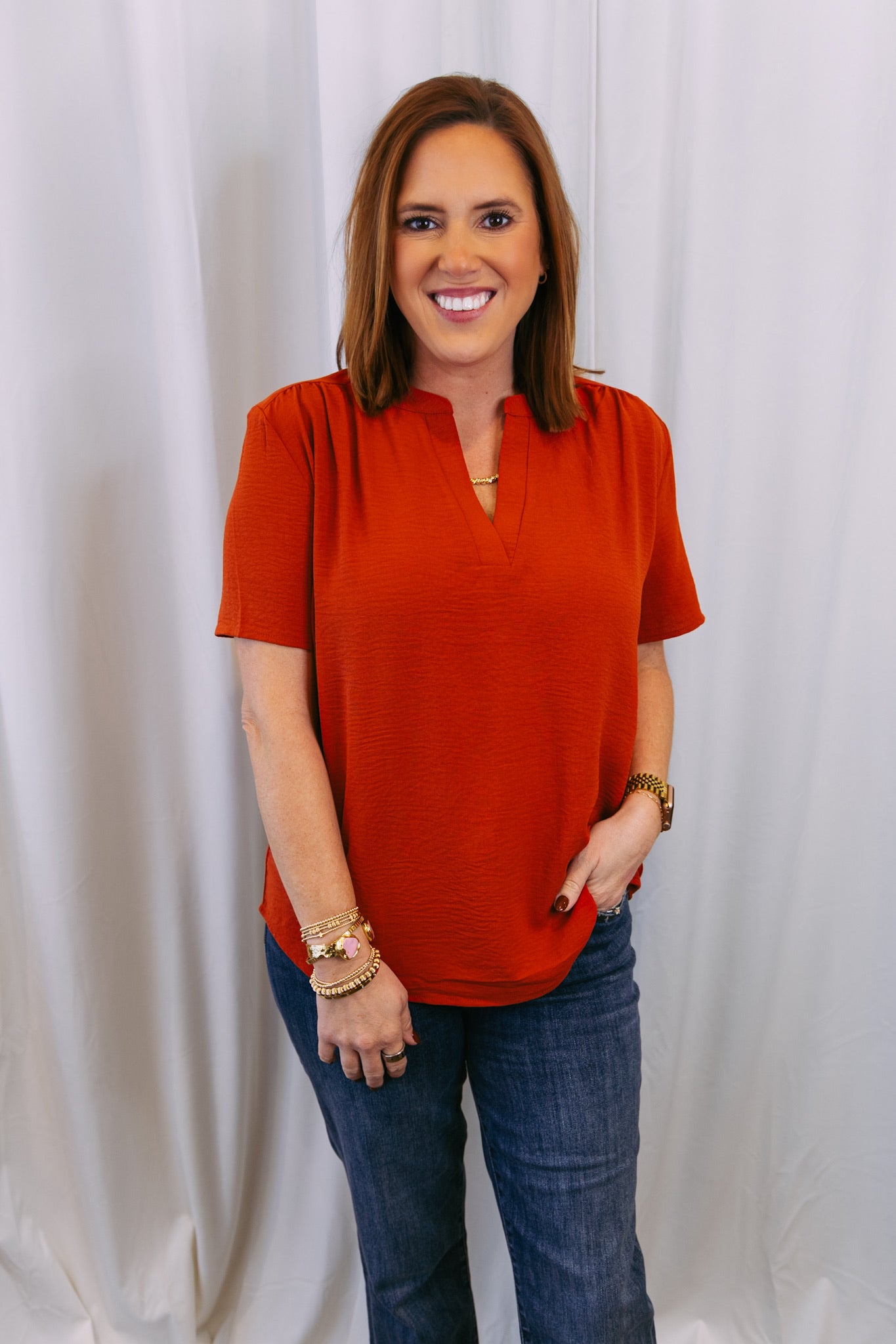 Woman wearing a rust-colored blouse and blue jeans against a white background