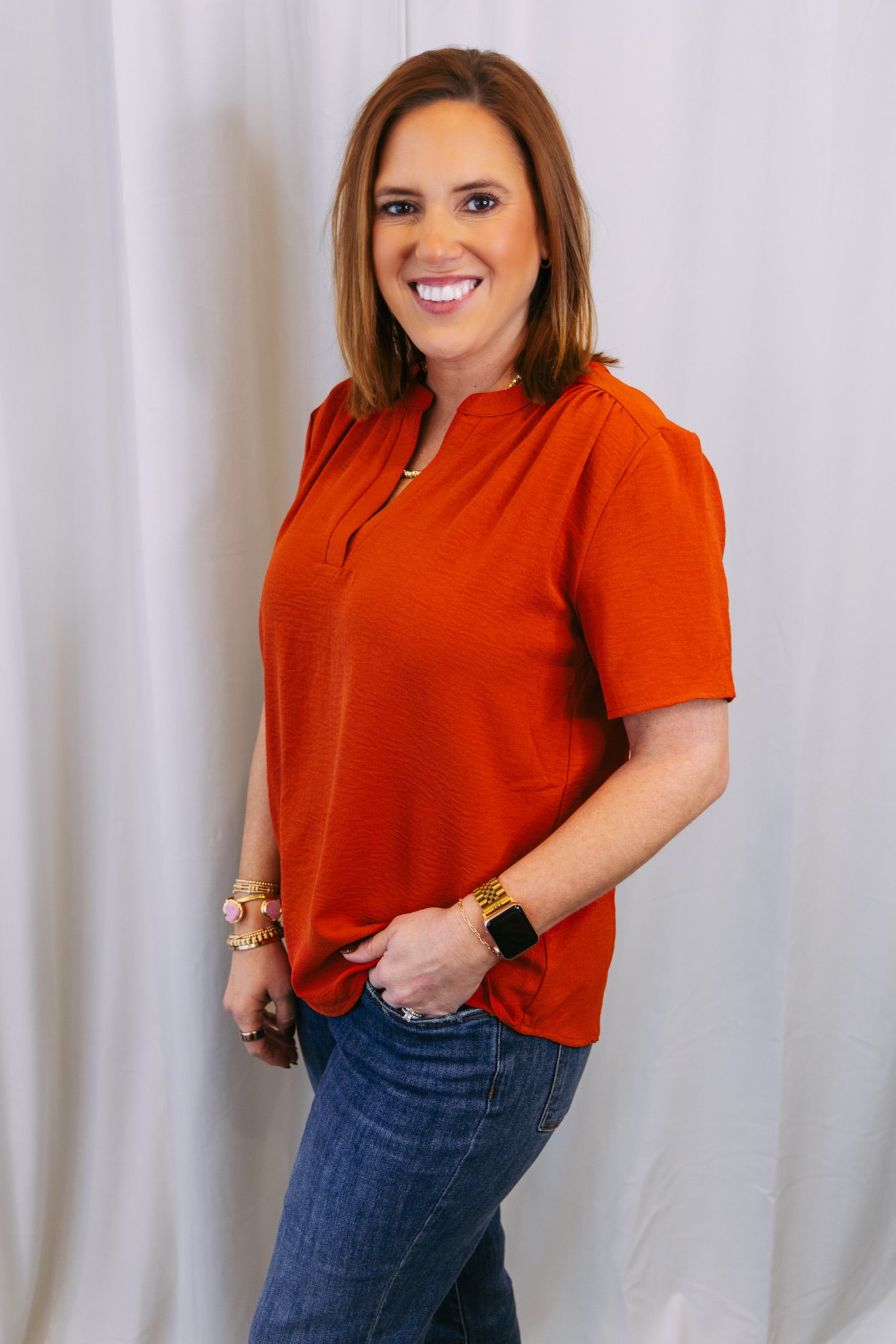 Woman wearing an orange top and blue jeans against a white background