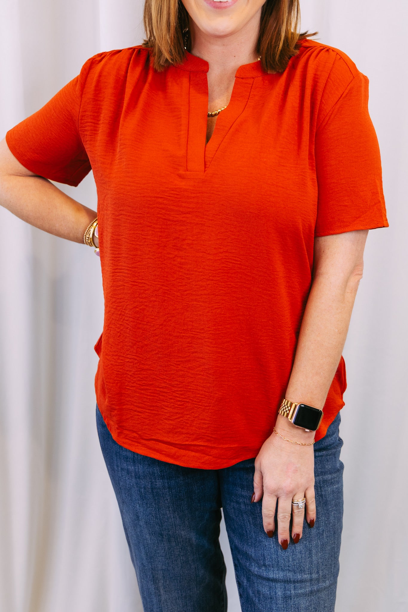 Person wearing an rust top and blue jeans against a white background