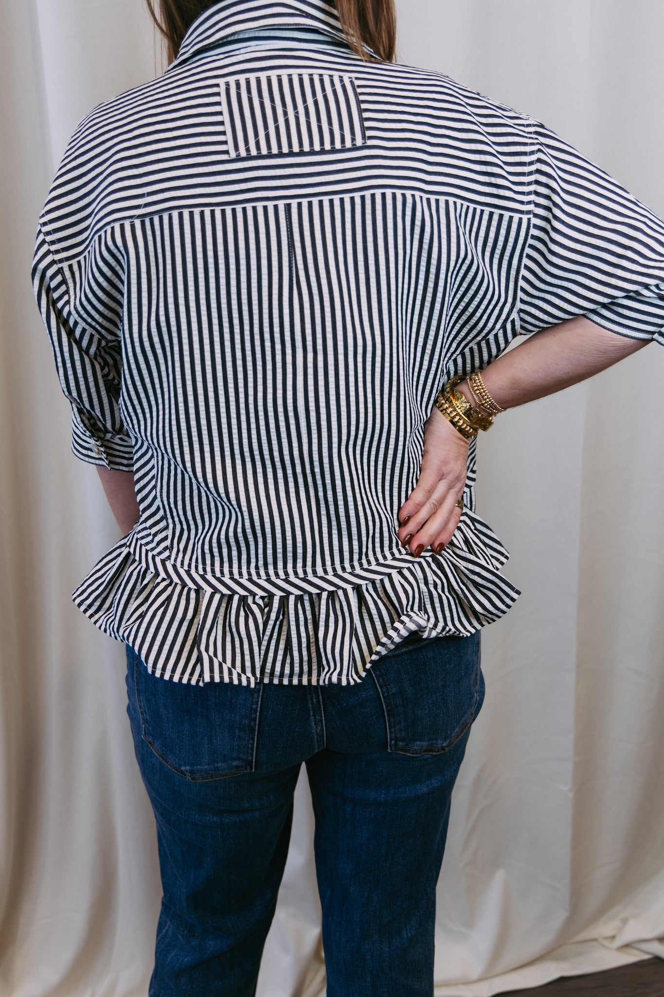 Person wearing a black and white striped shirt with ruffled bottom and blue jeans against a white curtain background