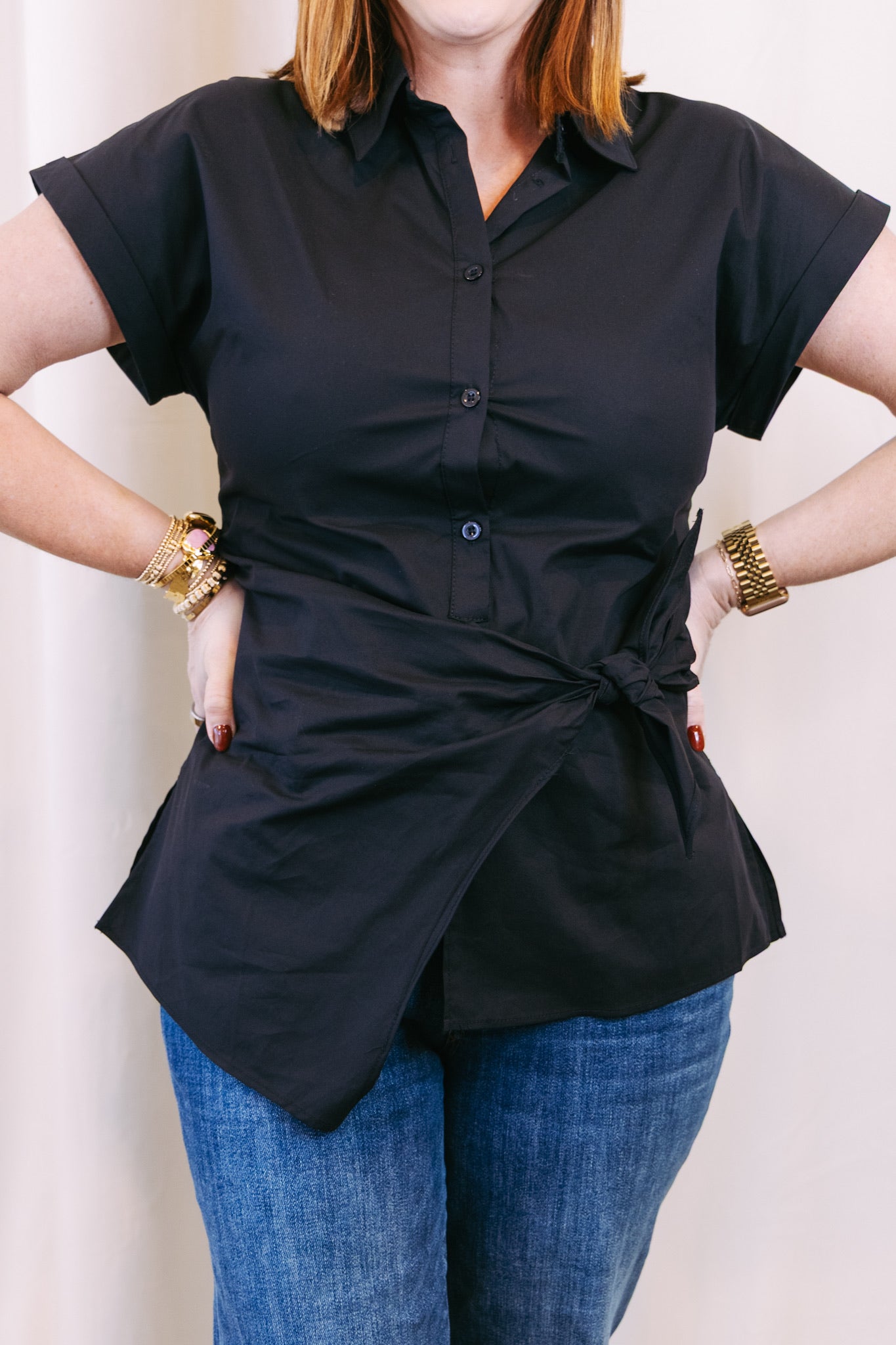 Person wearing a black short-sleeve blouse with a knot detail and blue jeans against a white background