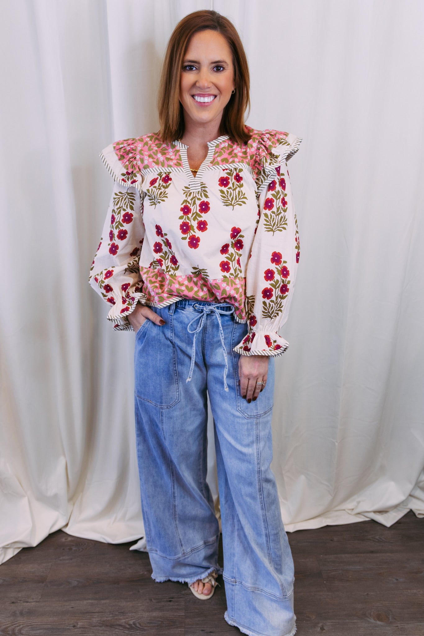 Woman wearing a floral blouse and jeans against a white curtain background