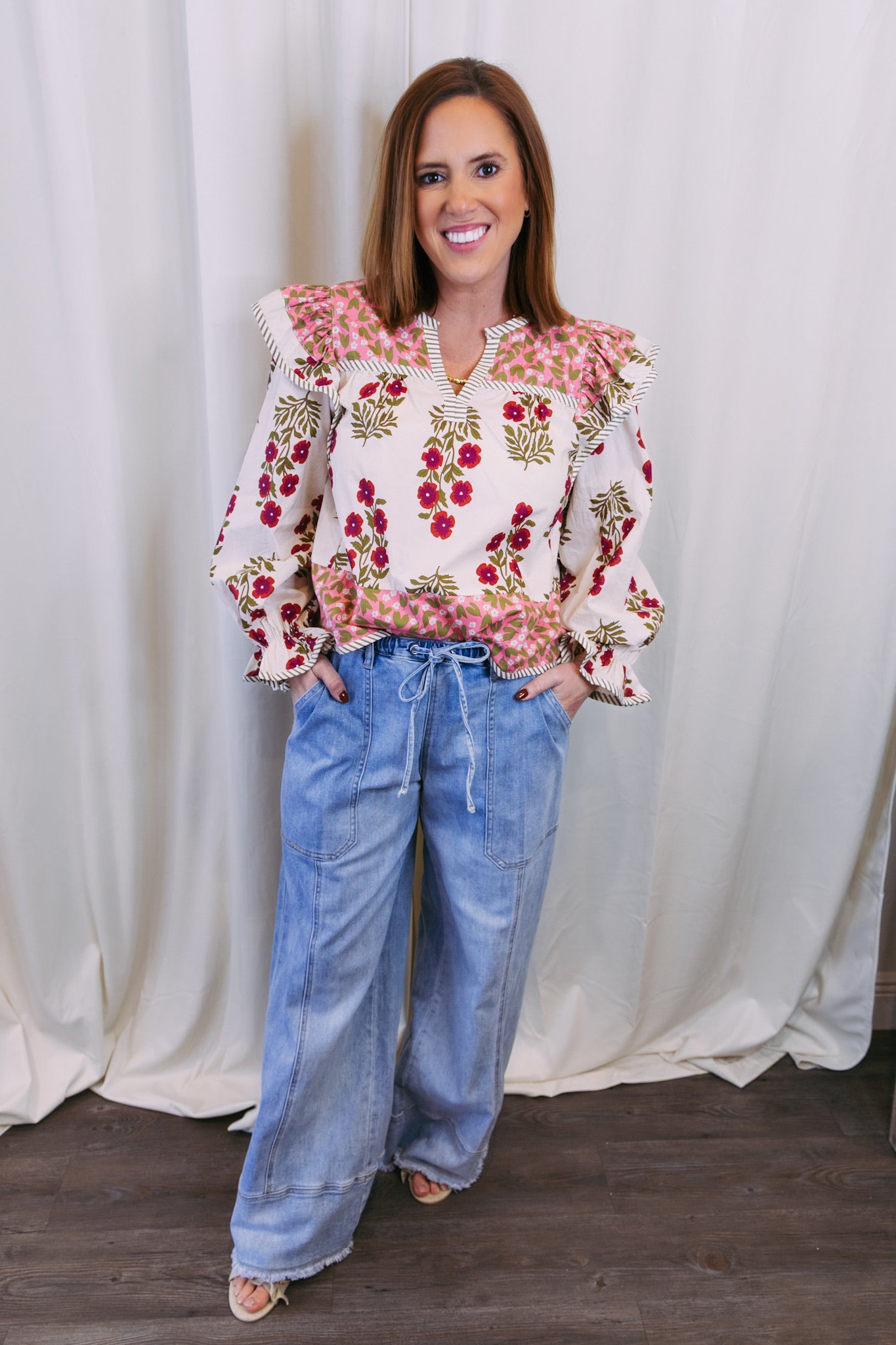 Woman wearing a floral blouse and blue jeans against a white curtain background