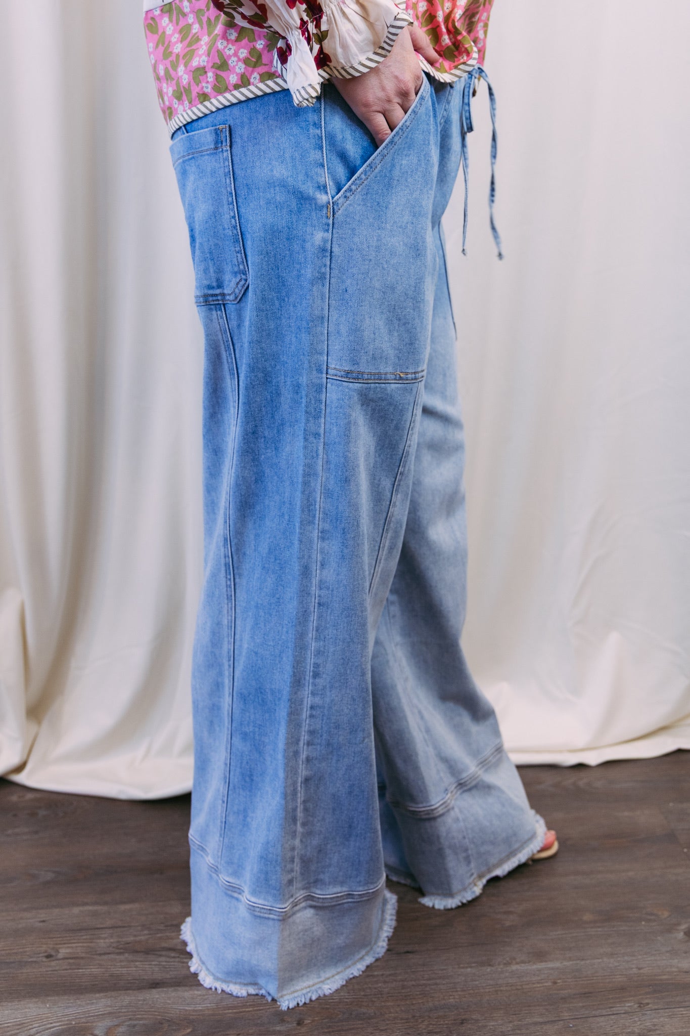 Person wearing light blue denim wide-leg pants with a white curtain background