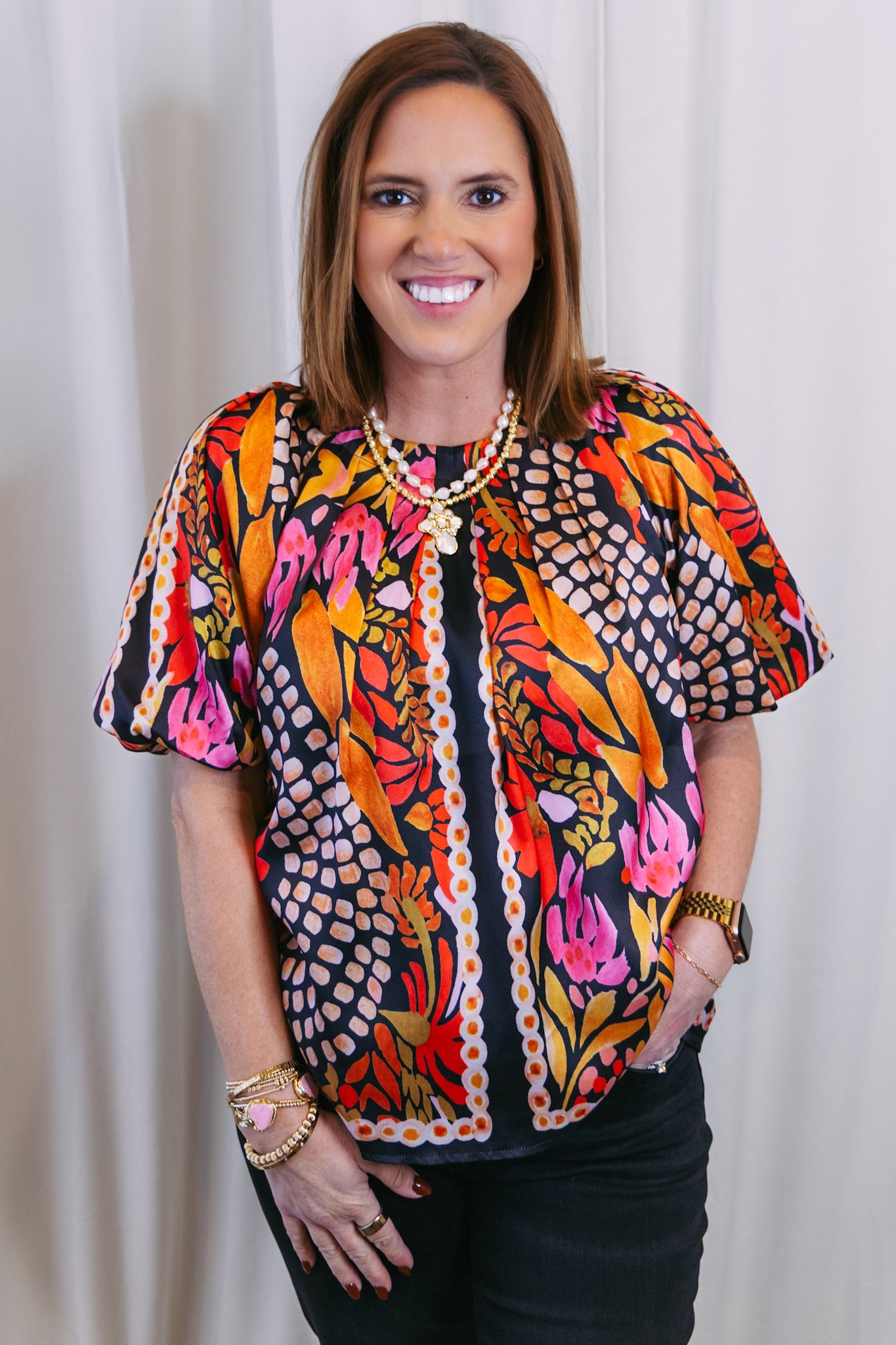 Woman wearing a colorful patterned blouse against a white curtain background