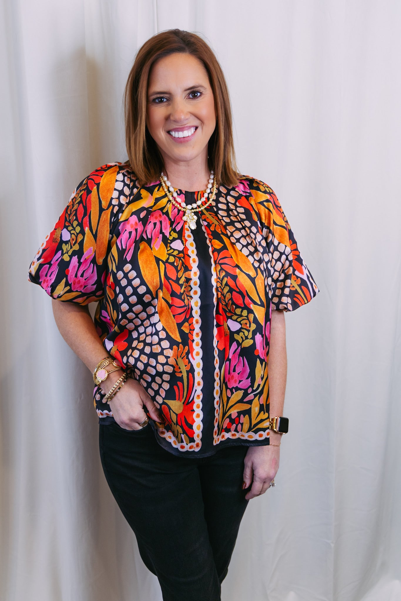Woman wearing a colorful patterned blouse against a white curtain background