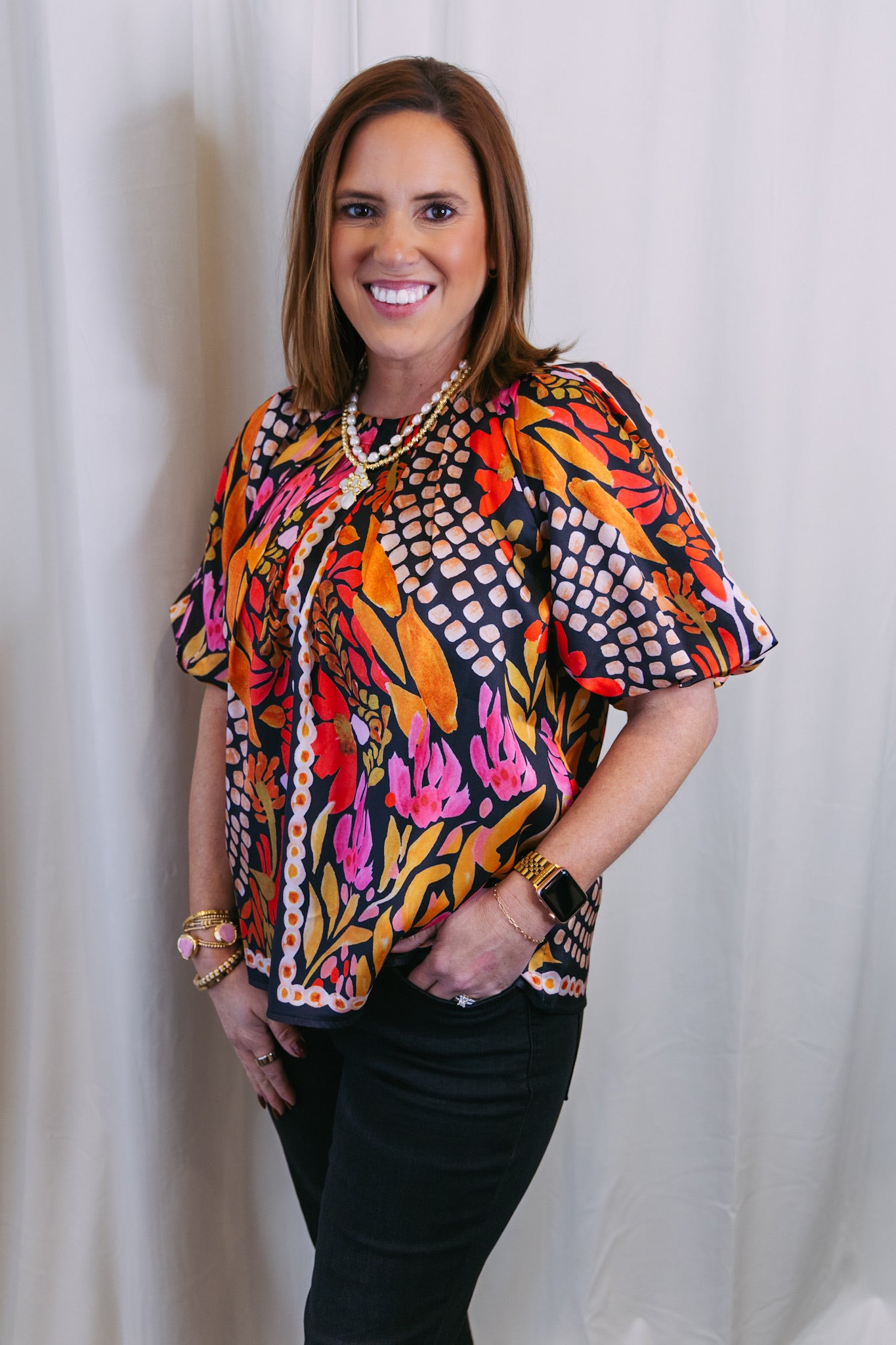 Woman wearing a colorful patterned blouse against a white curtain background