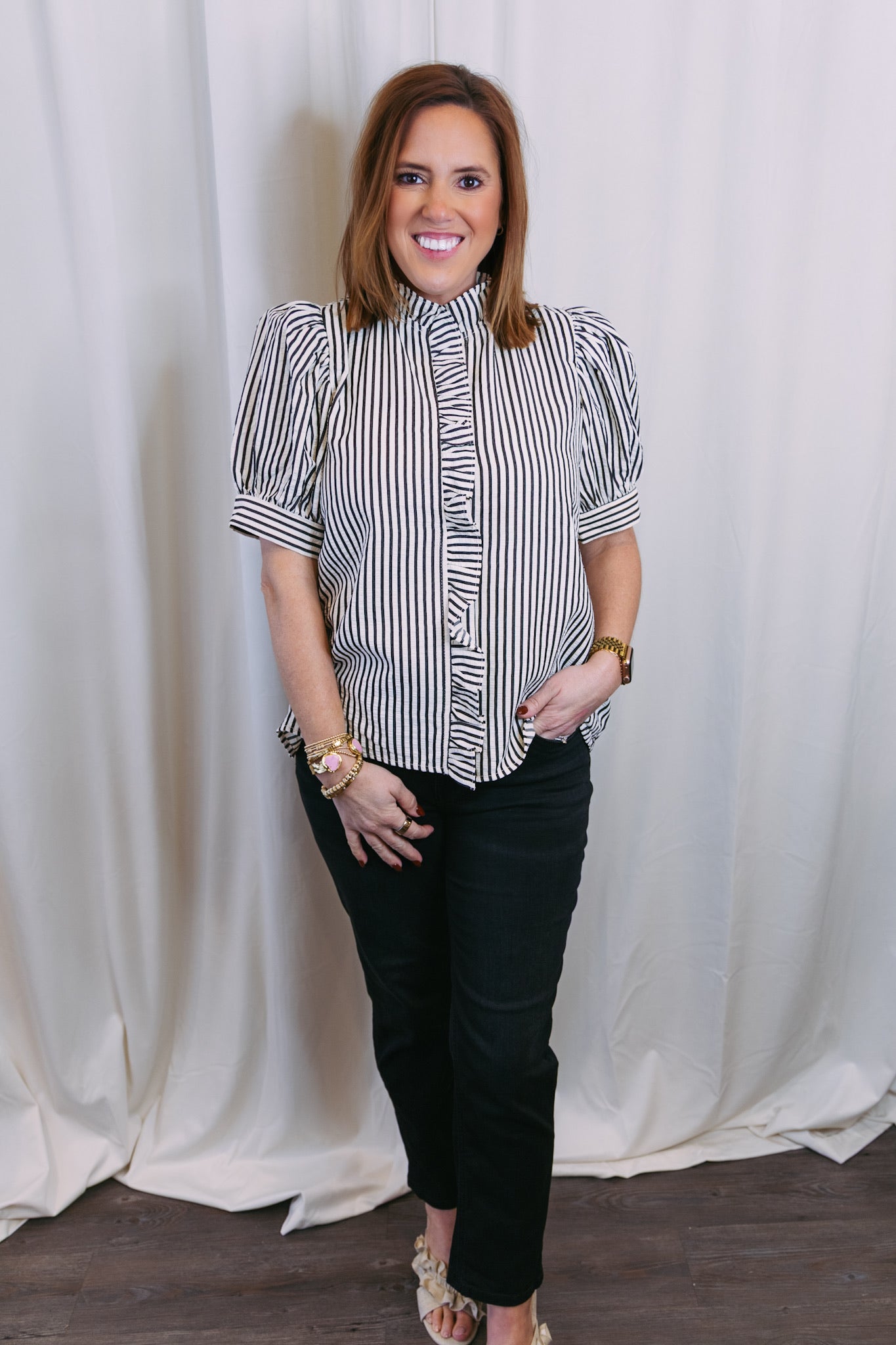Woman wearing a black and white striped shirt and black pants against a white curtain background