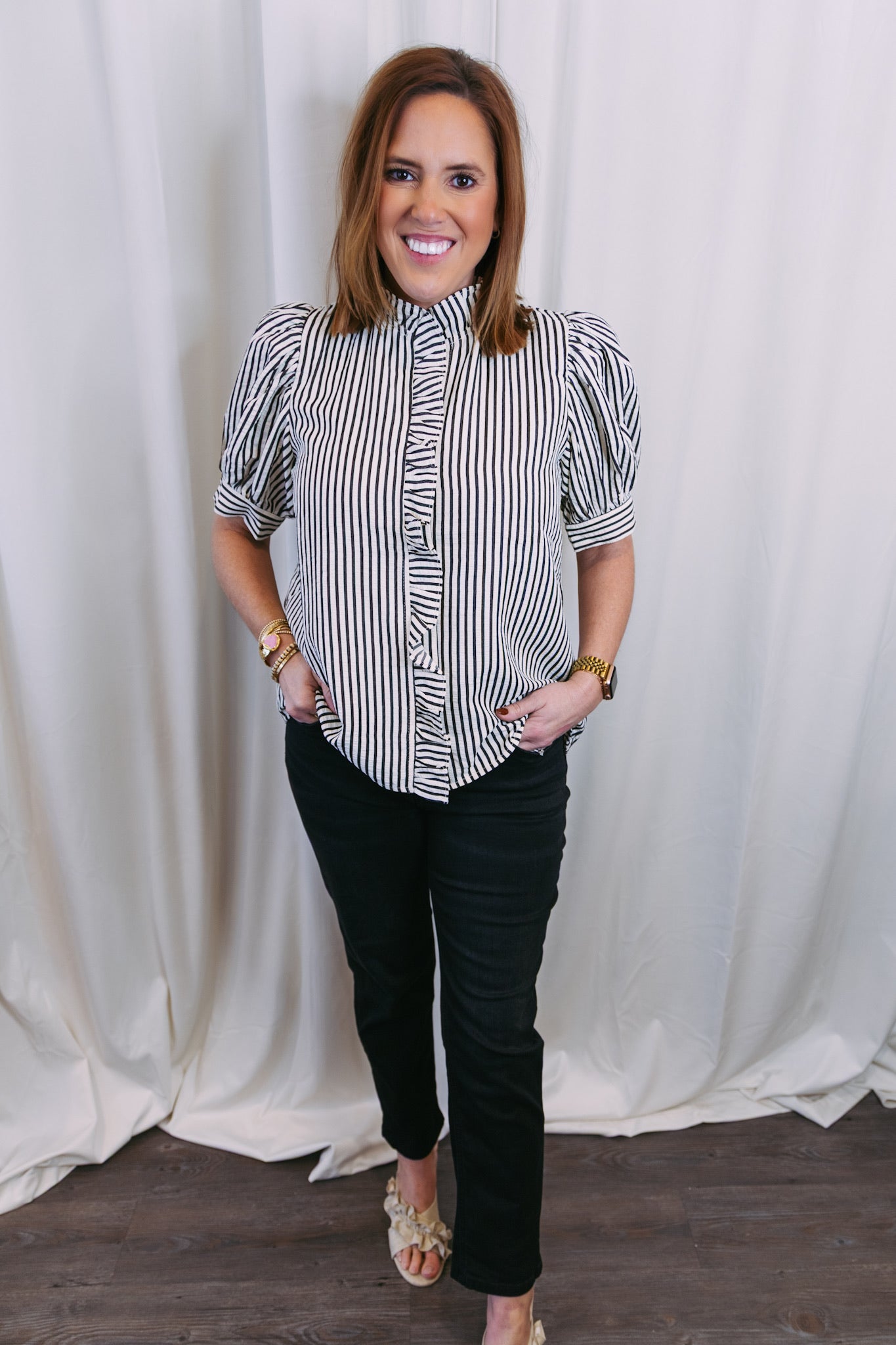 Woman wearing a black and white striped shirt and black pants against a white curtain background