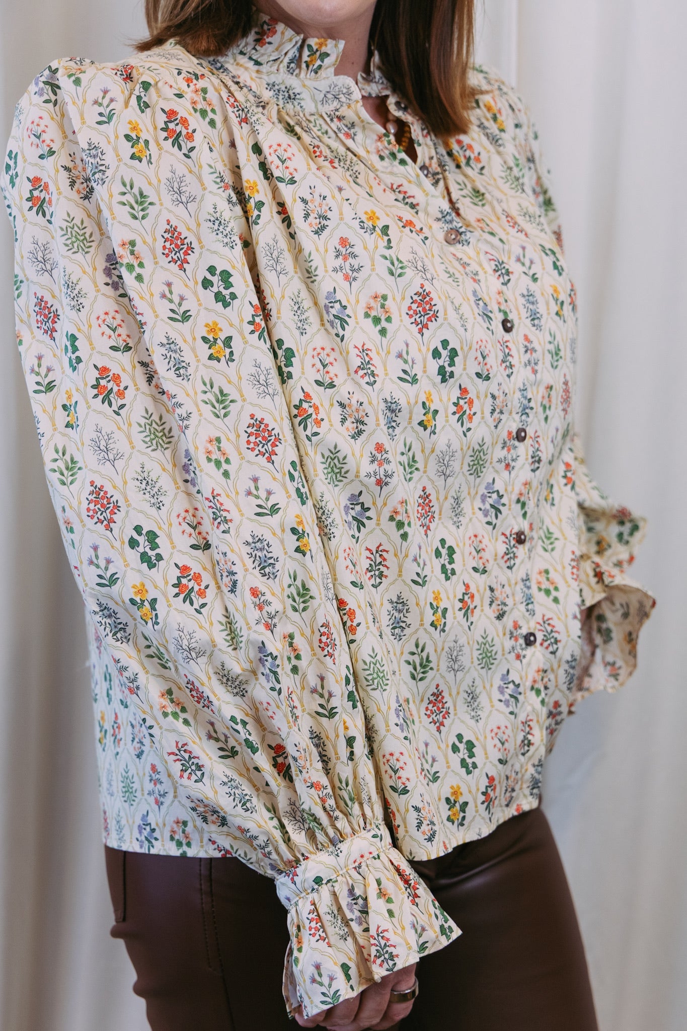 Floral patterned blouse with long sleeves and a high collar against a plain background