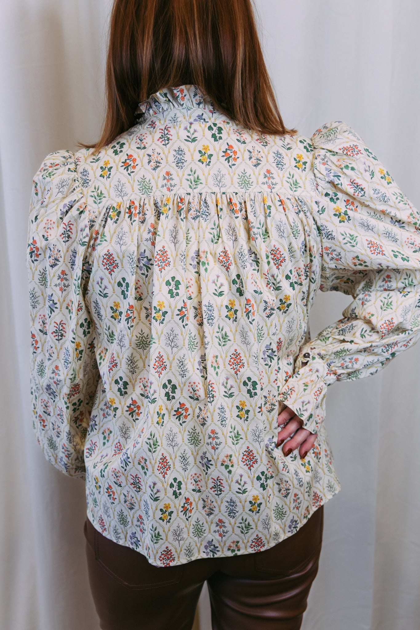 Person wearing a floral blouse with long sleeves against a plain background