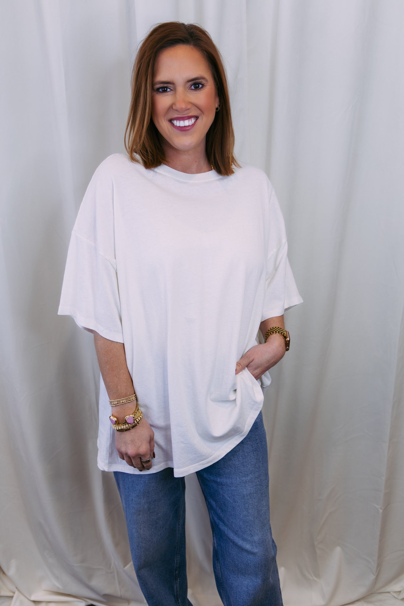 Woman wearing a white oversized top and blue jeans against a plain background