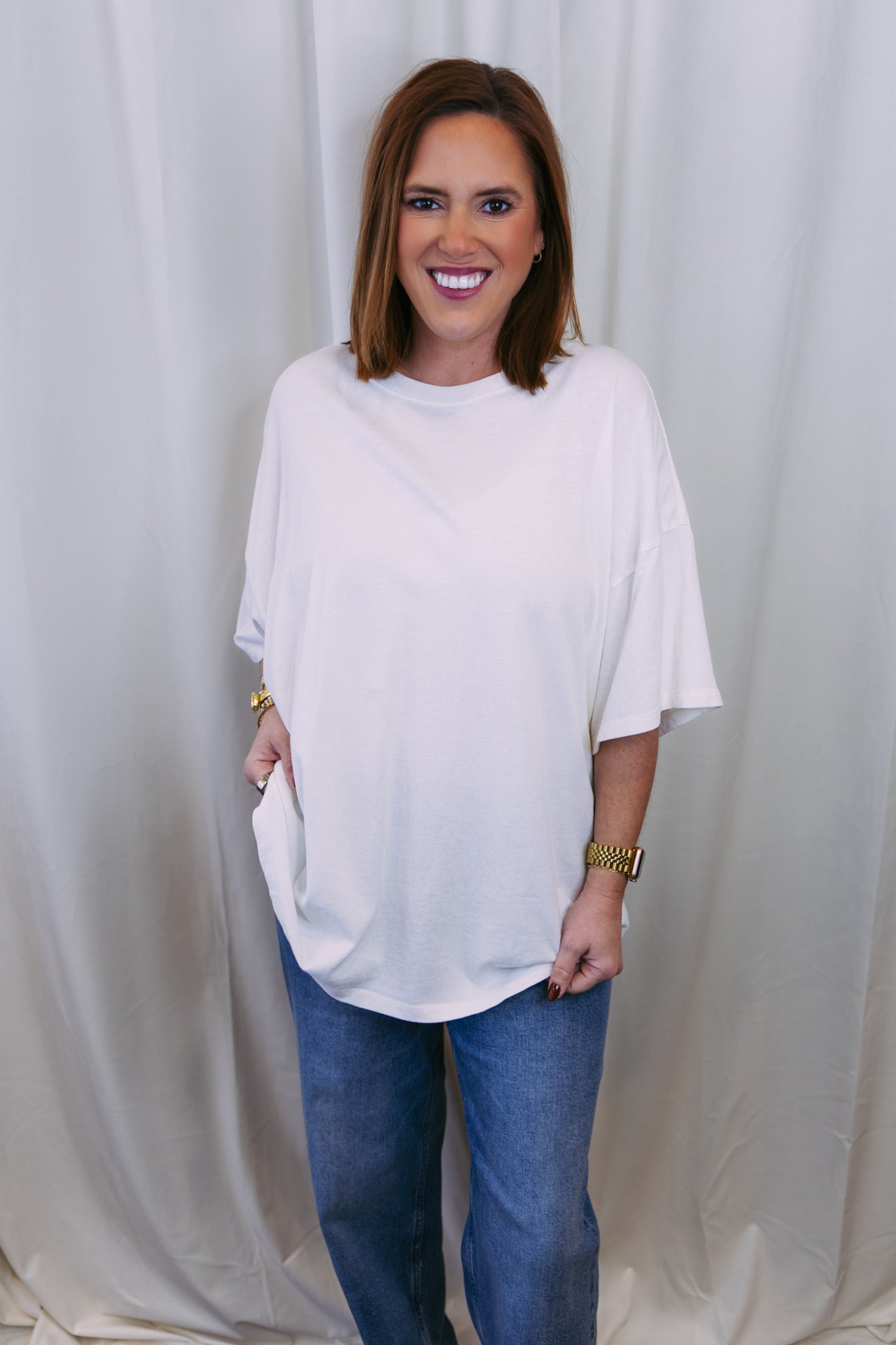 Woman wearing a white oversized shirt and blue jeans against a plain background