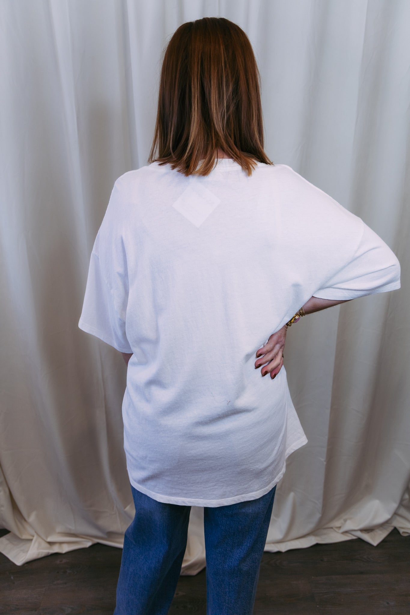 Person wearing a white oversized t-shirt and blue jeans against a plain background