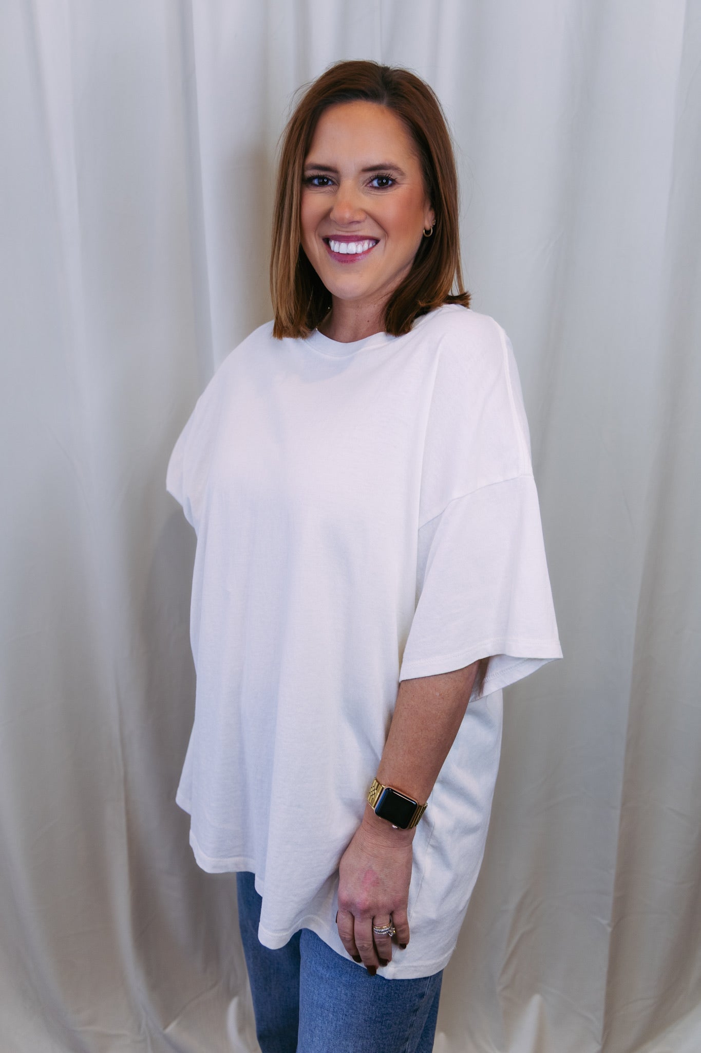 Woman wearing a white oversized shirt and blue jeans against a plain background