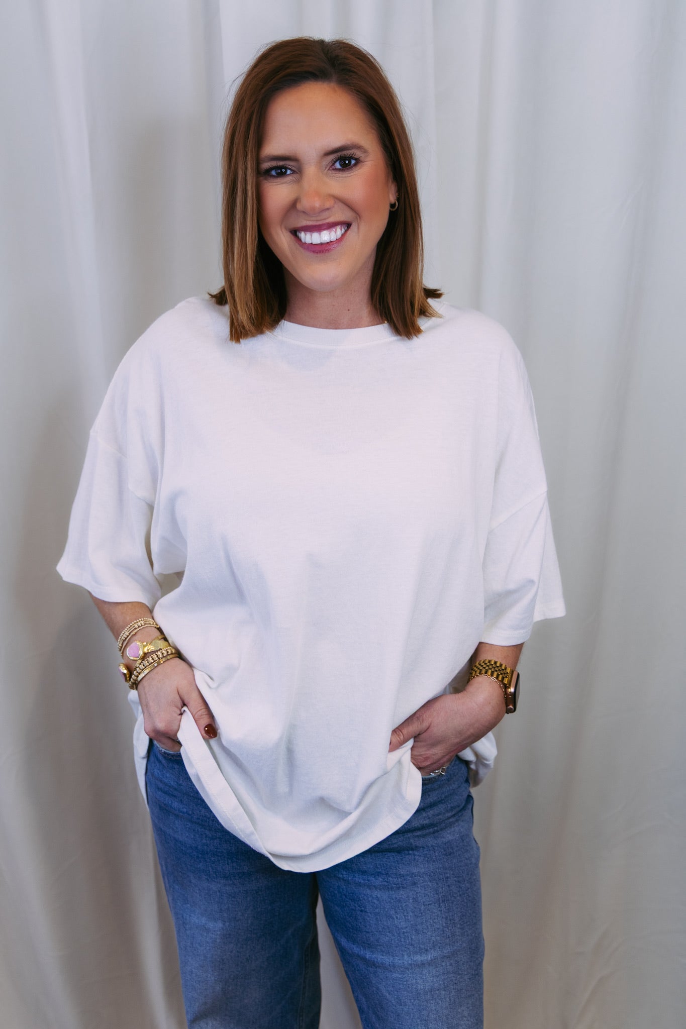Woman wearing a white oversized shirt and blue jeans against a plain background